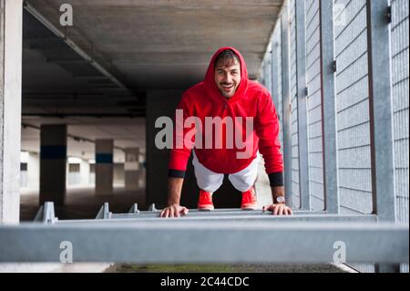 Porträt eines glücklichen jungen Mannes, der Liegestütze auf einem Parkplatz macht Stockfoto