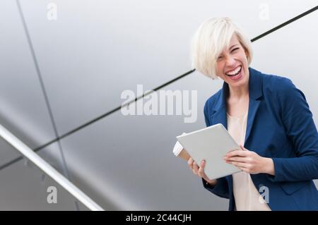 Porträt der lachenden blonden Geschäftsfrau mit Tablet und Kaffee zu gehen Stockfoto