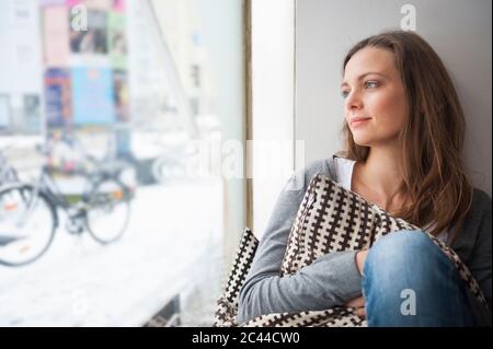 Porträt einer träumenden Frau in einem Café, die im Winter durch das Fenster schaut Stockfoto