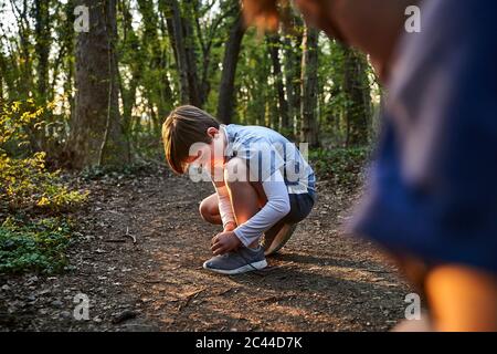 Seitenansicht des Jungen beim Knüpfen von Schnürsenkeln im Wald Stockfoto