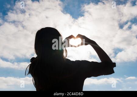Rückansicht der Frau, die mit ihren Händen das Herz formt Stockfoto