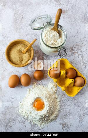 Eigelb in Mehl, Hühnereier, Schüssel mit braunem Zucker und Glas Mehl Stockfoto