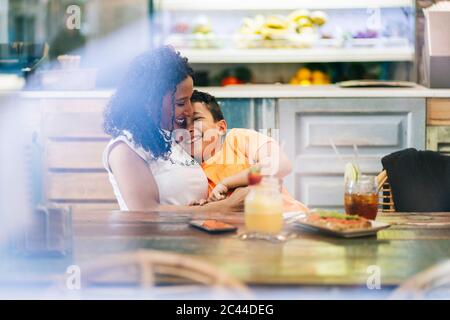Junge Frau genießen, während umarmt Sohn im Restaurant Stockfoto