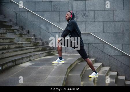 Junger Jogger, der sein Bein in der Stadt streckt Stockfoto