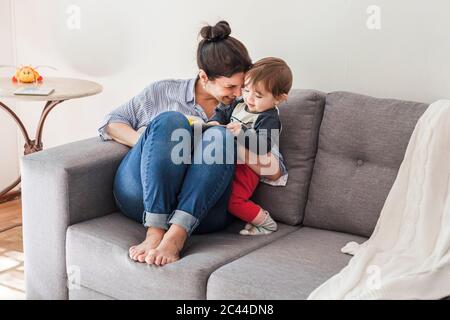 Glückliche Mutter sitzt auf der Couch und kuschelt ihren kleinen Sohn Stockfoto