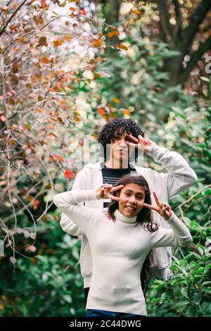 Bruder und Schwester zeigen Friedenszeichen, während sie inmitten von Pflanzen im Park stehen Stockfoto