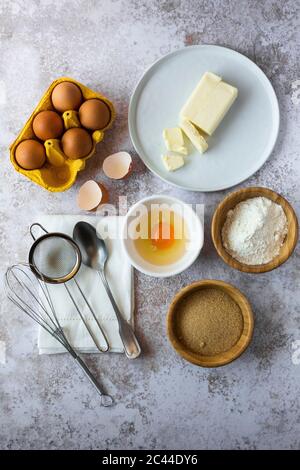 Hühnereier, Butter, Mehl, brauner Zucker, Serviette, Löffel, Sieb und Drahtquirl Stockfoto