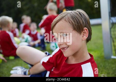 Porträt des verspielten Jungen mit Fußballmannschaft im Hintergrund auf dem Feld Stockfoto