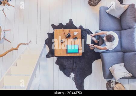 Direkt über der Mitte der erwachsenen Mann sitzt auf einem Sofa beim surfen net durch digitale Tablette im Wohnzimmer zu Hause Stockfoto