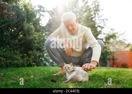 Älterer Mann, der Katze im Garten putzt Stockfoto