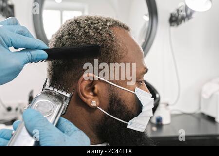 Friseur trägt chirurgische Maske und Handschuhe tun Haar des Kunden Stockfoto