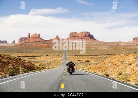 Rückansicht des Mannes, der auf der Wüstenstraße Motorrad reitet, Monument Valley Tribal Park, Utah, USA Stockfoto