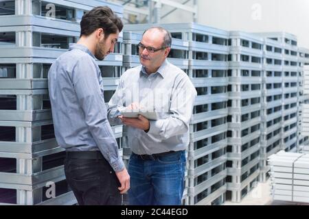 Zwei Geschäftsleute mit Tablet, die in einer Fabrik diskutieren Stockfoto