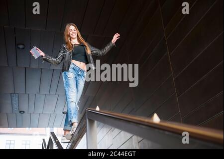 Glückliche junge Frau balanciert auf Geländer, während sie Musik im unterirdischen Gang hört Stockfoto