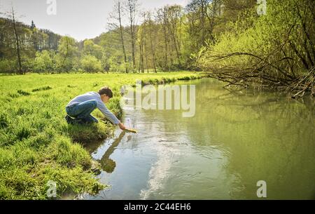 Boy setzt sein selbst-made Spielzeug Boot in Fluss im Wald an sonnigen Tag Stockfoto