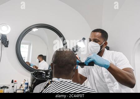 Friseur trägt chirurgische Maske und Handschuhe schneiden Haare des Kunden Stockfoto