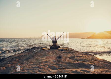 Reife Frau, die abends am felsigen Strand Yoga praktiziert Stockfoto