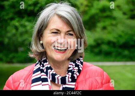 Fröhliche ältere Frau trägt Schalldämpfer und Jacke im Park Stockfoto