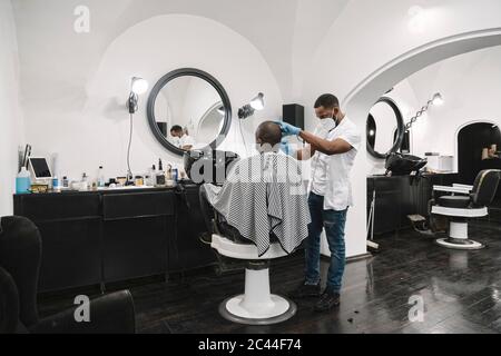 Friseur trägt chirurgische Maske und Handschuhe schneiden Haare des Kunden Stockfoto