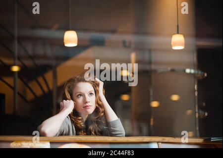 Nachdenkliche Frau, die sich durch das Fenster im Café auf den Tisch lehnte Stockfoto