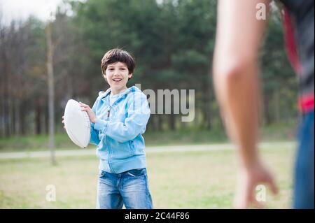 Glücklicher Junge, der Rugby mit Vater im Park spielt Stockfoto
