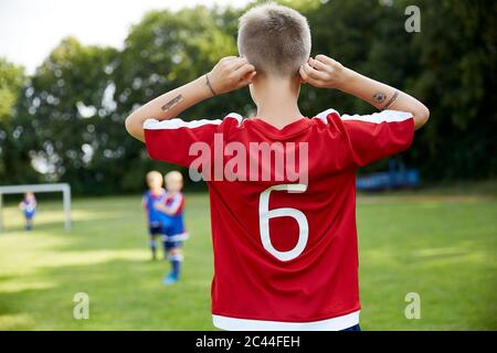 Fußballjunge hält Ohren, während er auf dem Feld steht Stockfoto