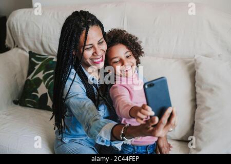 Portrait von glücklicher Mutter und ihrer kleinen Tochter, die Selfie mit dem Smartphone auf der Couch macht Stockfoto