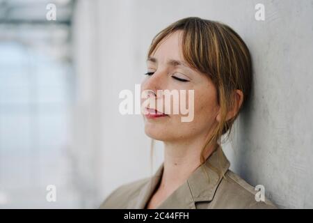 Porträt einer Geschäftsfrau mit geschlossenen Augen, die an einer Betonwand lehnt Stockfoto