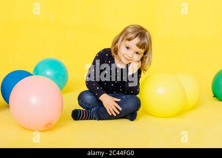 Portrait von lächelnd niedlichen Mädchen mit bunten Ballons vor gelbem Hintergrund sitzen Stockfoto