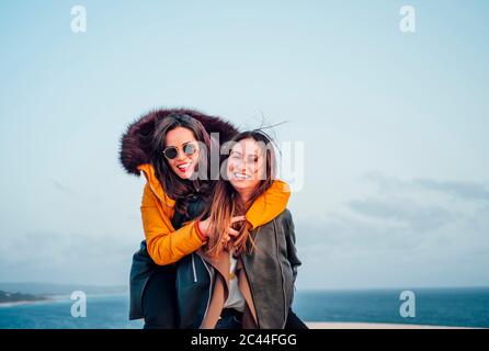 Huckepack-Frau fröhliche Freundin beim Genießen am Strand gegen Himmel in Tarifa, Spanien Stockfoto