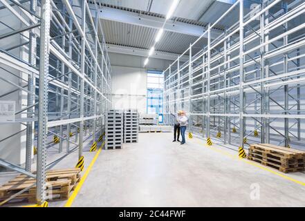 Zwei Männer mit Schutzmützen reden im Lagerhaus einer Fabrik Stockfoto