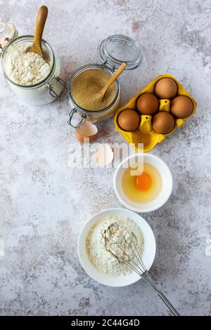 Drahtbesen, Hühnereier und Gläser Mehl und brauner Zucker Stockfoto