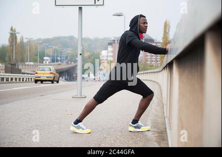 Junger Jogger, der sein Bein in der Stadt streckt Stockfoto