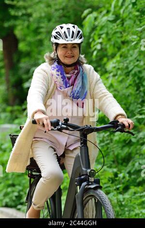 Glückliche ältere Frau, die auf dem Fußweg im Park mit dem Elektrofahrrad fährt Stockfoto