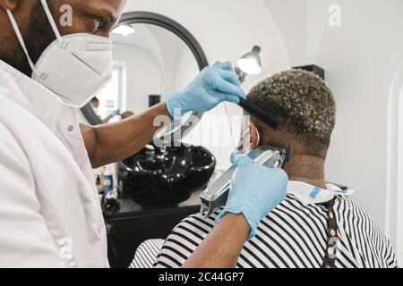 Friseur trägt chirurgische Maske und Handschuhe rasieren Haare des Kunden Stockfoto