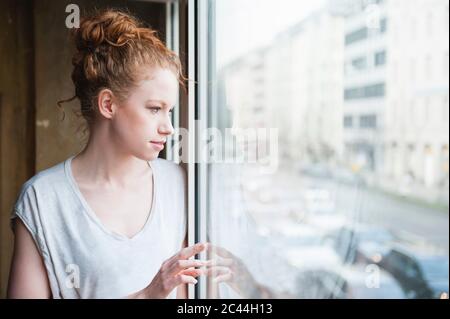 Nachdenkliche junge Frau Blick durch Fenster zu Hause Stockfoto