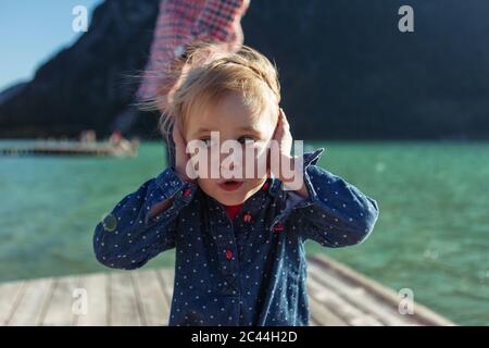 Nettes Mädchen, das Ohren bedeckt, während Vater im Hintergrund auf der Promenade am Achensee, Bundesland Tirol, Österreich Stockfoto