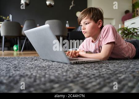 Junge auf dem Boden liegend, am Laptop arbeitend Stockfoto