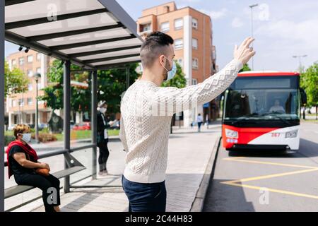 Mann mit Schutzmaske steht an der Bushaltestelle mit Taxi, Spanien Stockfoto