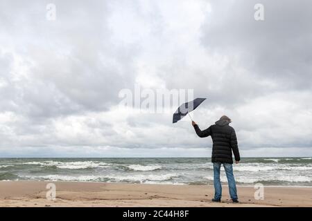 Russland, Kaliningrad Oblast, Zelenogradsk, Mann auf sandigen Küstenstrand mit Sonnenschirm in der Hand stehen Stockfoto