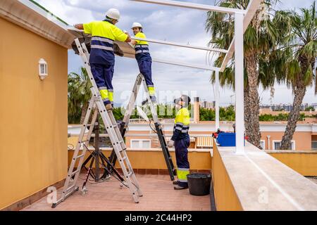 Mann, der Kollegen beim Installieren von Solarzellen auf dem Dach ansieht, während er auf dem Balkon steht Stockfoto