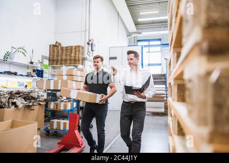 Zwei Männer mit Paket und Klemmbrett im Lager einer Fabrik Stockfoto