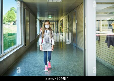 Mädchen trägt Maske zu Fuß auf Schulflur Stockfoto