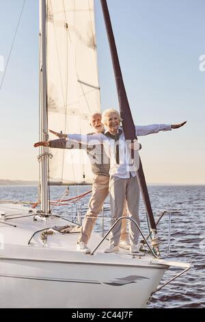 Gegen den Wind. Glückliches Senior-Paar auf der Seite des Segelbootes oder Yacht Deck schwimmend im Meer. Mann und Frau strecken Hände gegen die Stockfoto