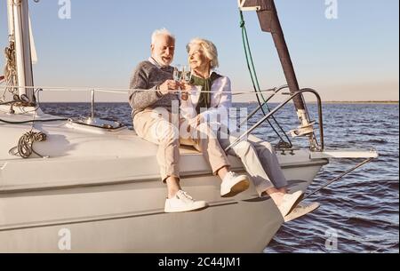 Gute Stimmung. Glückliches Senior-Paar auf der Seite des Segelbootes oder Yacht Deck schwimmend im Meer sitzen. Mann und Frau trinken Wein oder Champagner, genießen die Stockfoto