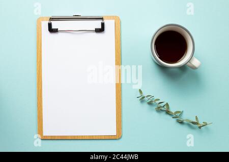 Arbeitsbereich. Zwischenablage und leeres Papierblatt mit Tasse Kaffee auf blauem Hintergrund. Draufsicht Stockfoto