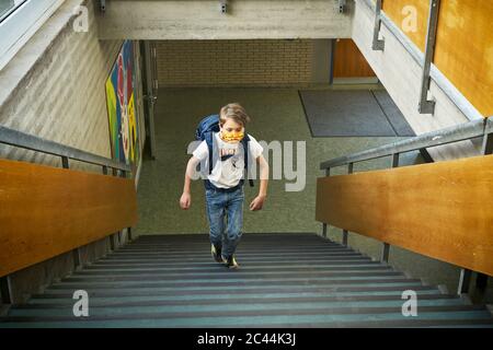 Junge in der Schule, der die Treppe hinauf ging, trägt eine Maske Stockfoto