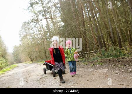 Zwei kleine Schwestern ziehen Trolley auf Waldweg Stockfoto