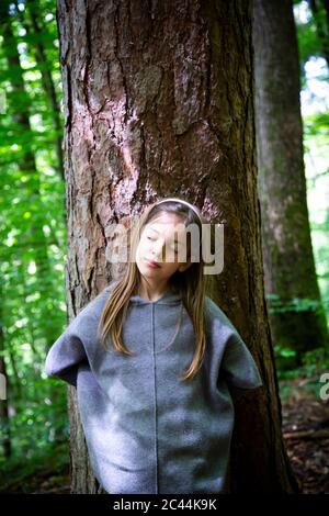 Junges Mädchen mit geschlossenen Augen steht gegen Baumstamm im Wald Stockfoto