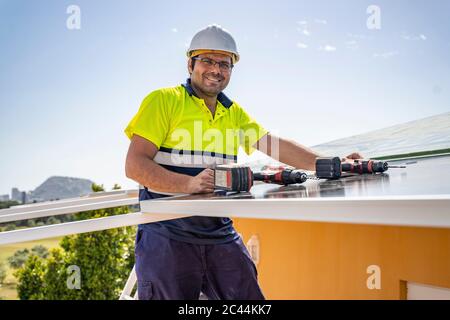 Portrait von lächelndem reifen Techniker, der Solarpanel auf dem Hausdach gegen den Himmel installiert Stockfoto